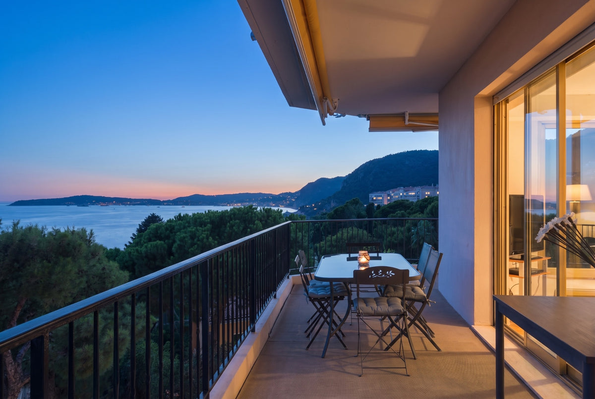 Exemple de séance crépuscule : terrasse avec vue mer à l'heure bleue, lumière intérieure chaude, appartement à Cap-d'Ail, Côte d'Azur